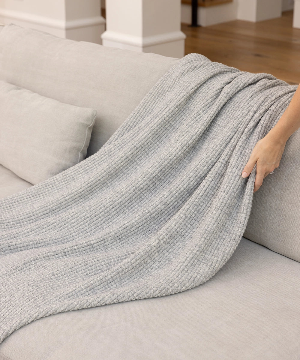 A woman draping a Moonstone AU Baby Adult Popcorn blanket over the back of a grey couch.