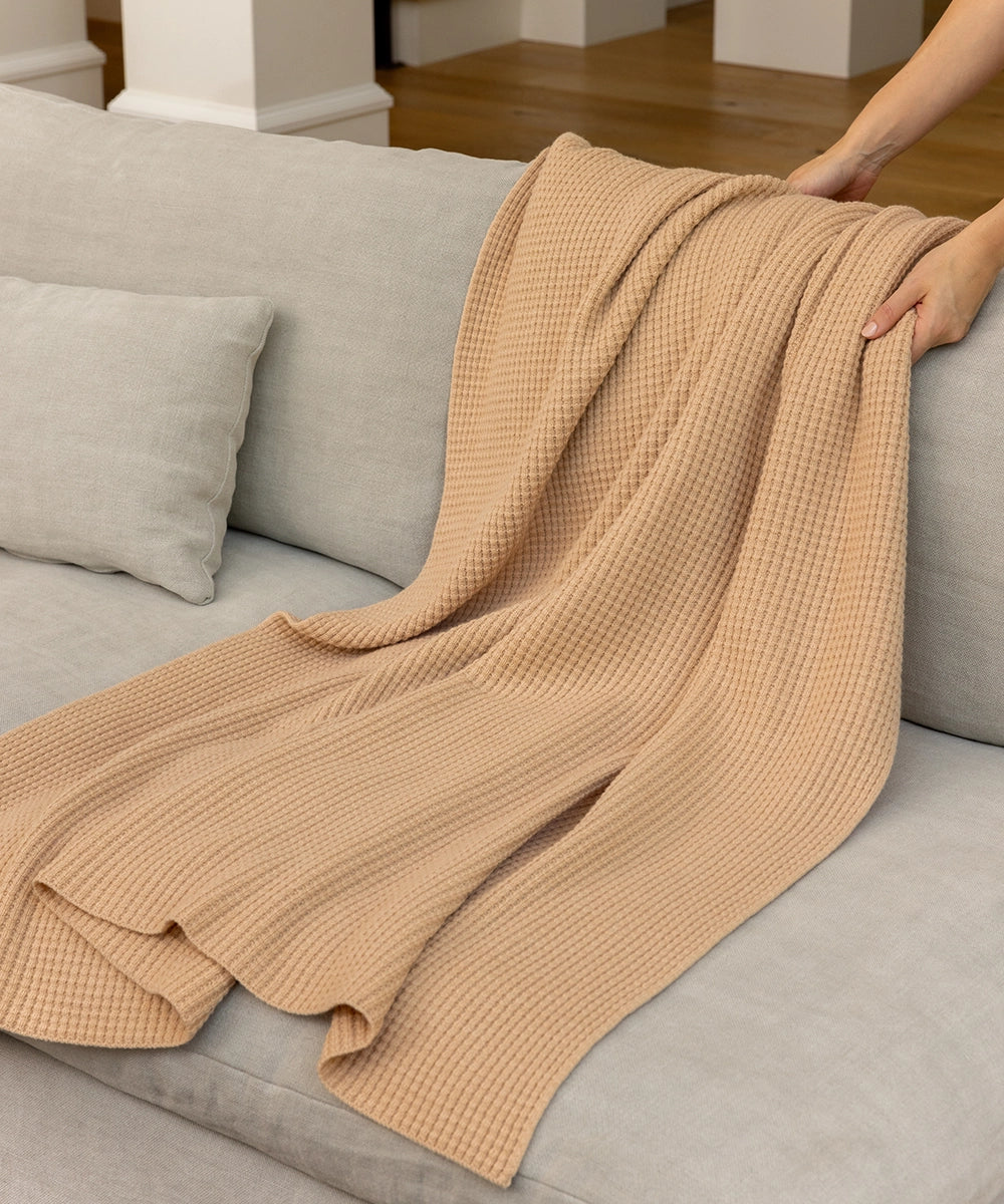 A woman draping an AU Baby Popcorn blanket in Henna over the back of a grey couch.