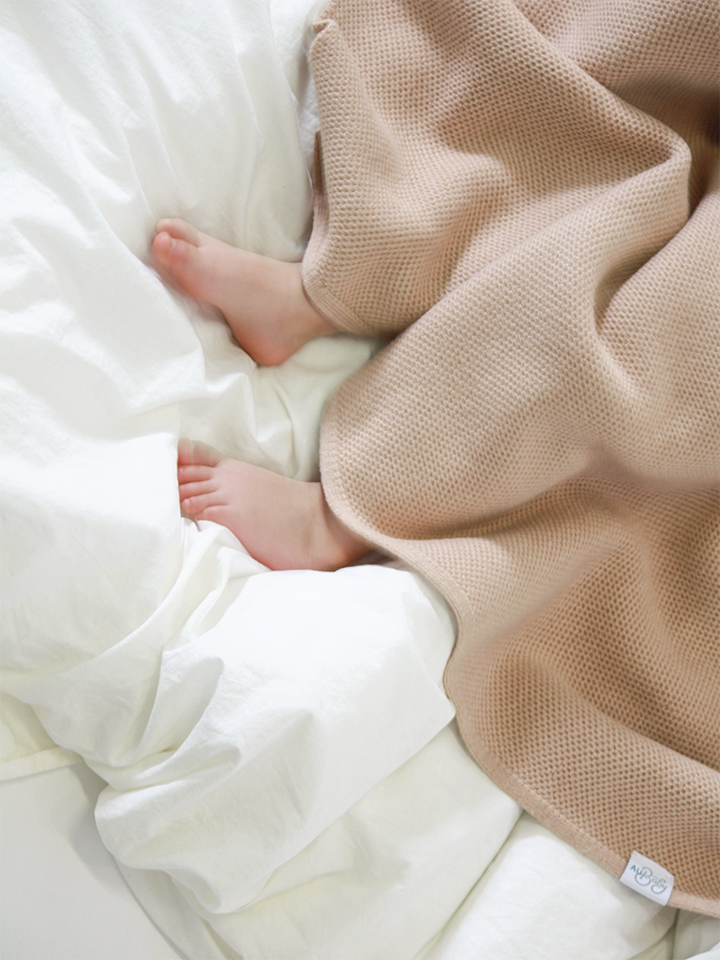 Baby girl's feet cuddled in a beige, plant-dyed baby blanket. Luxury, non-toxic, natural merino blanket made in the USA.