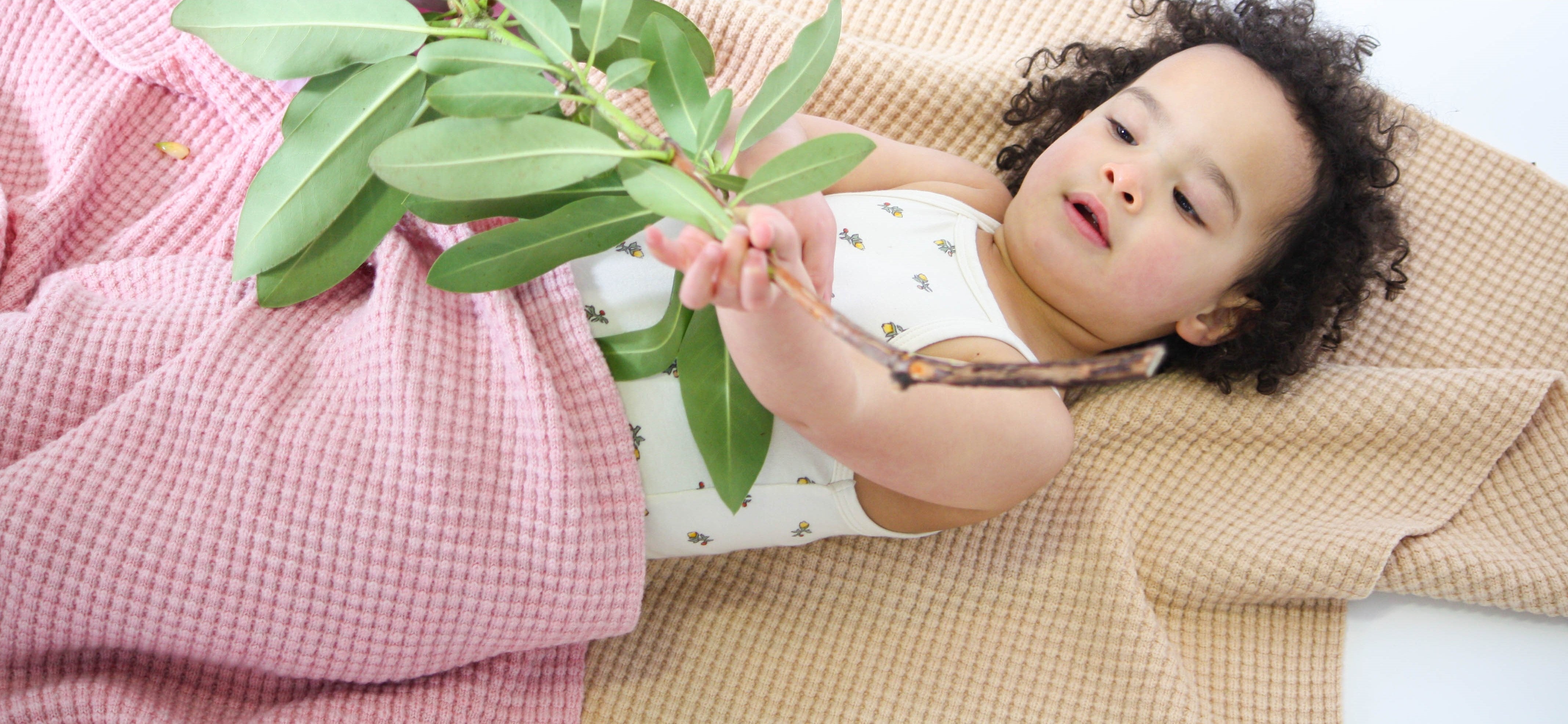 Toddler relaxing with pink and beige merino AU Baby Popcorn blankets.
