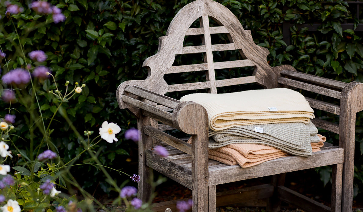 AU Baby's plant-dyed merino adult blankets stacked on a chair in the garden.