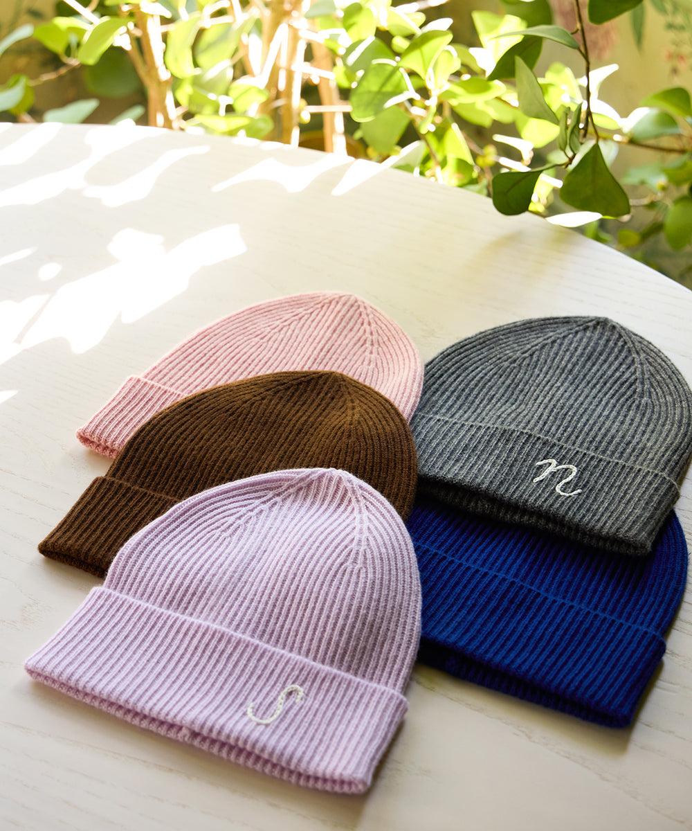 Assortment of AU Baby Cashmere Cloud merino wool and cashmere beanies in pastel pink, chocolate brown, charcoal grey, Lavender, and Cobalt blue, including embroidered initials.