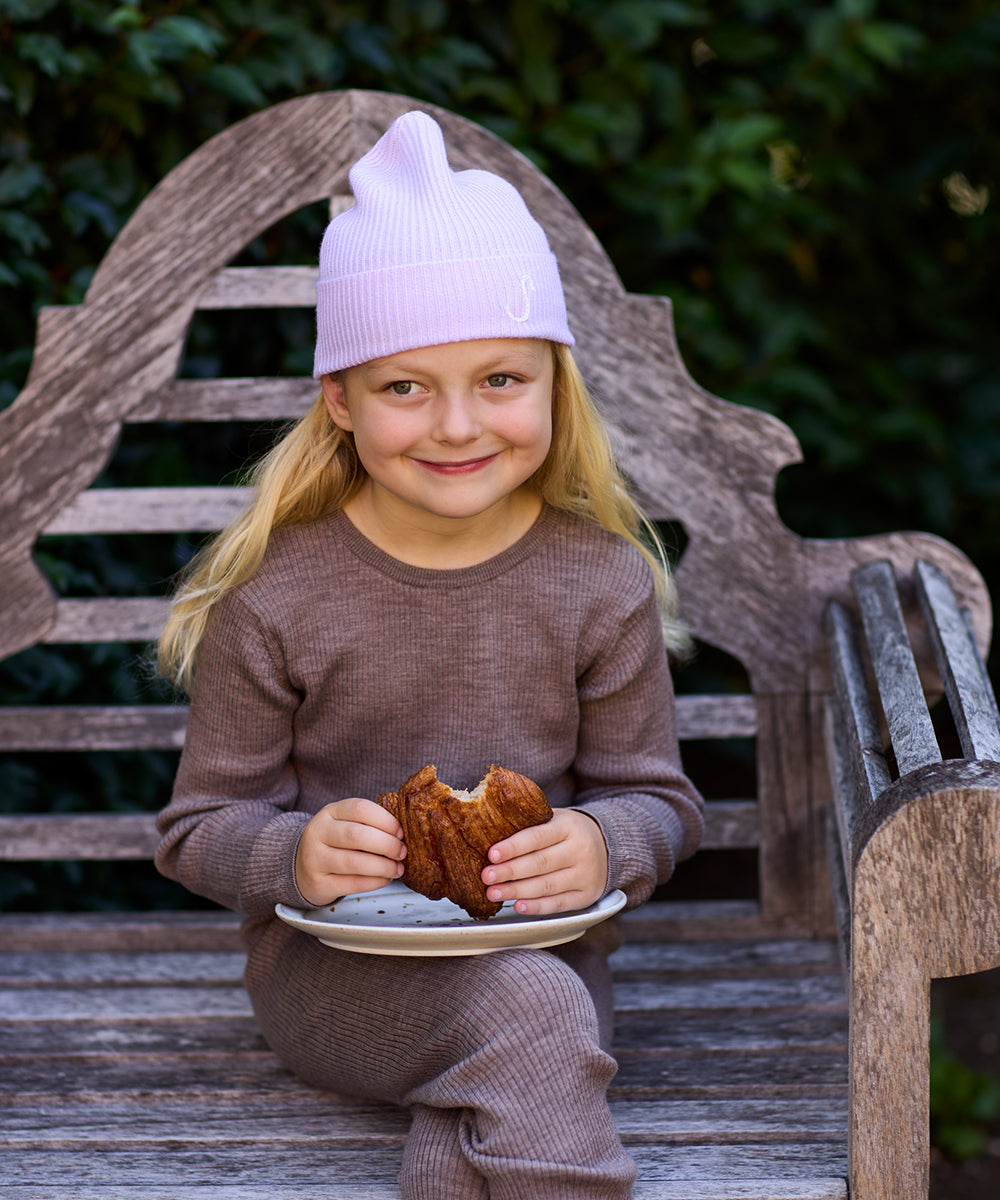 Smiling young girl wearing a personalized Lavender merino wool and cashmere beanie while sitting on a wooden garden bench.