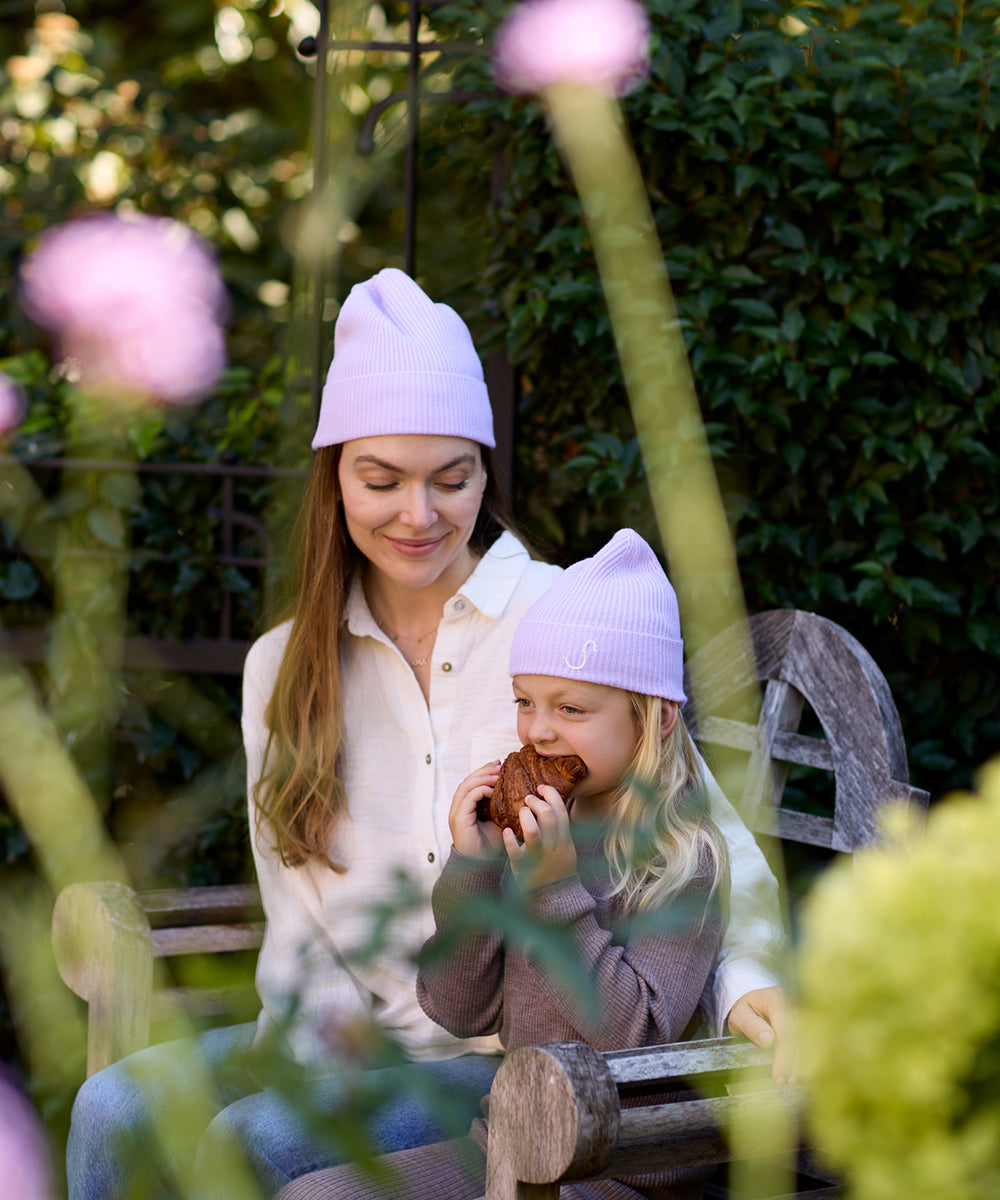 Mother and daughter wearing matching Lavender merino wool and cashmere beanies while relaxing together on a garden bench.