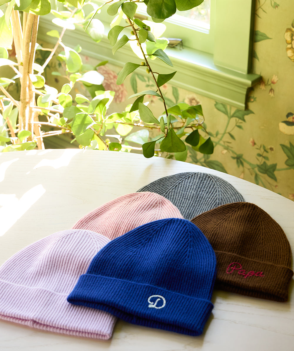 Flat lay of AU Baby merino wool and cashmere beanies in five colors, featuring embroidered initials and a personalized name.