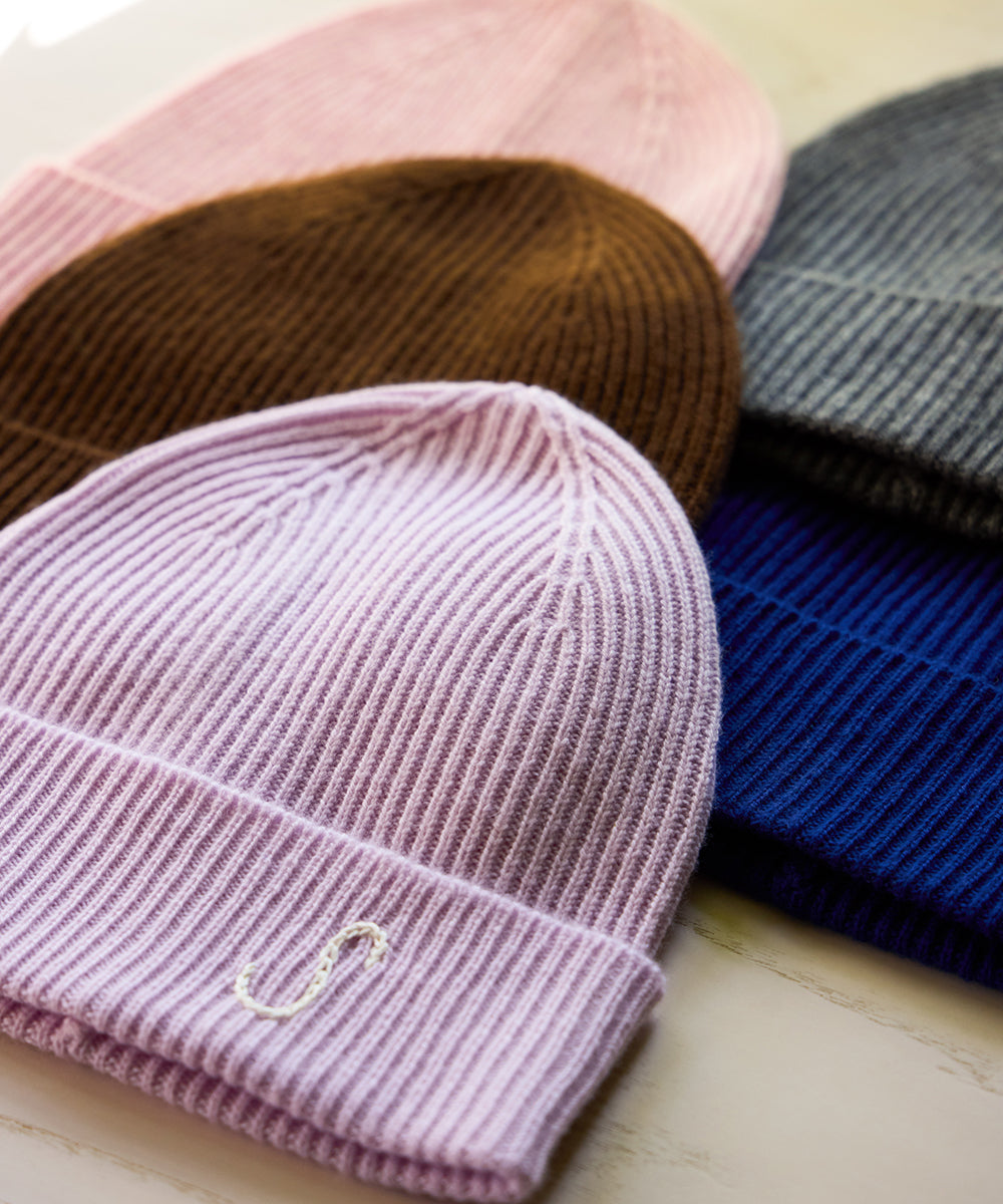Assortment of AU Baby Cashmere Cloud merino wool and cashmere beanies in pastel pink, chocolate brown, charcoal grey, Lavender, and Cobalt blue, including embroidered initials.