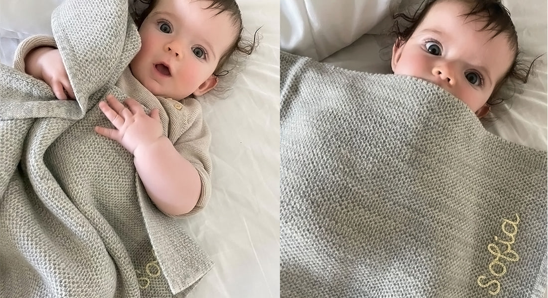 Baby girl cuddling with an embroidered grey AU Baby Sawa blanket.