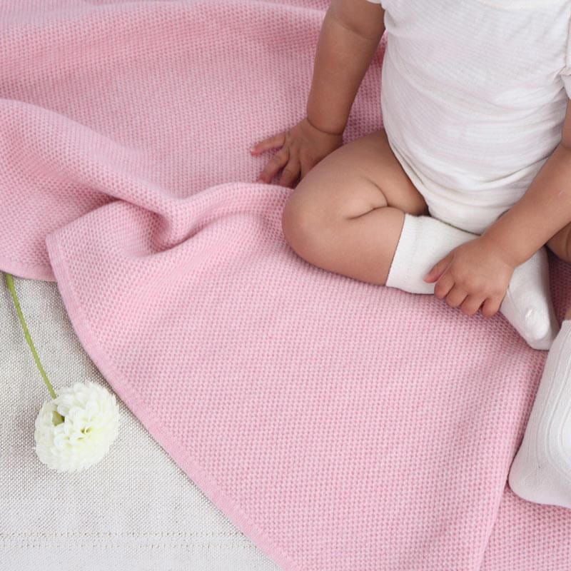 Baby girl sitting on AU Baby Sawa blanket in Pink Quartz. Non-toxic, natural baby blanket.